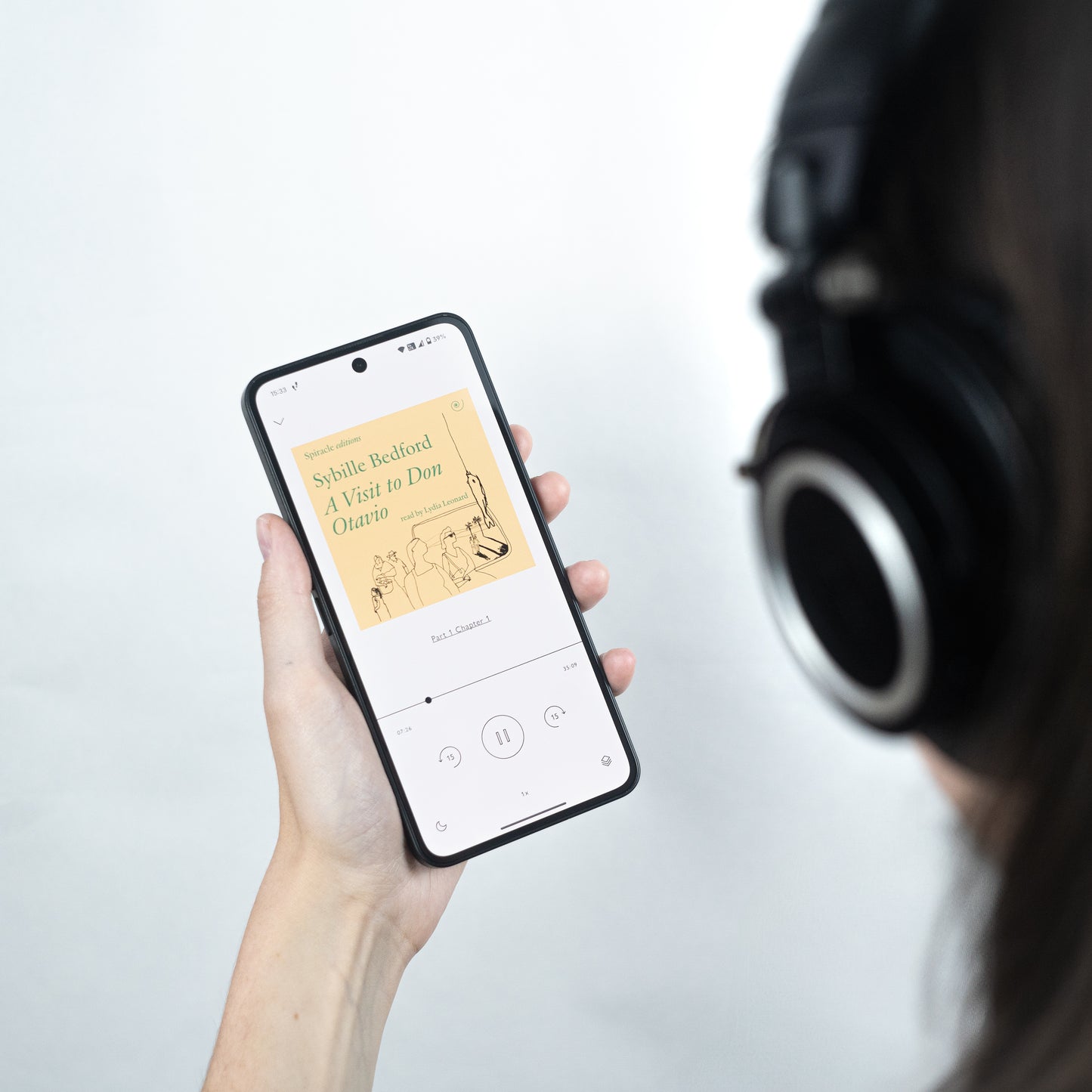 Person holding a smartphone with a music app and wearing headphones on a light gray background