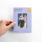 Hand holding a book titled 'Mrs Dalloway' by Virginia Woolf on a white background